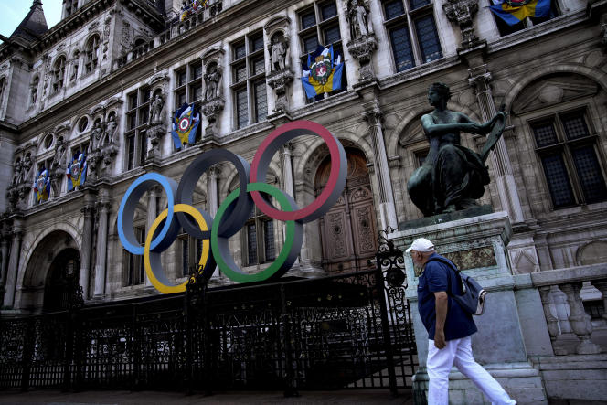 A man walks past the Olympic rings in front of the Paris City Hall one year until the Paris 2024 Olympic Games opening ceremony, Wednesday, July 26, 2023. (AP Photo/Christophe Ena)